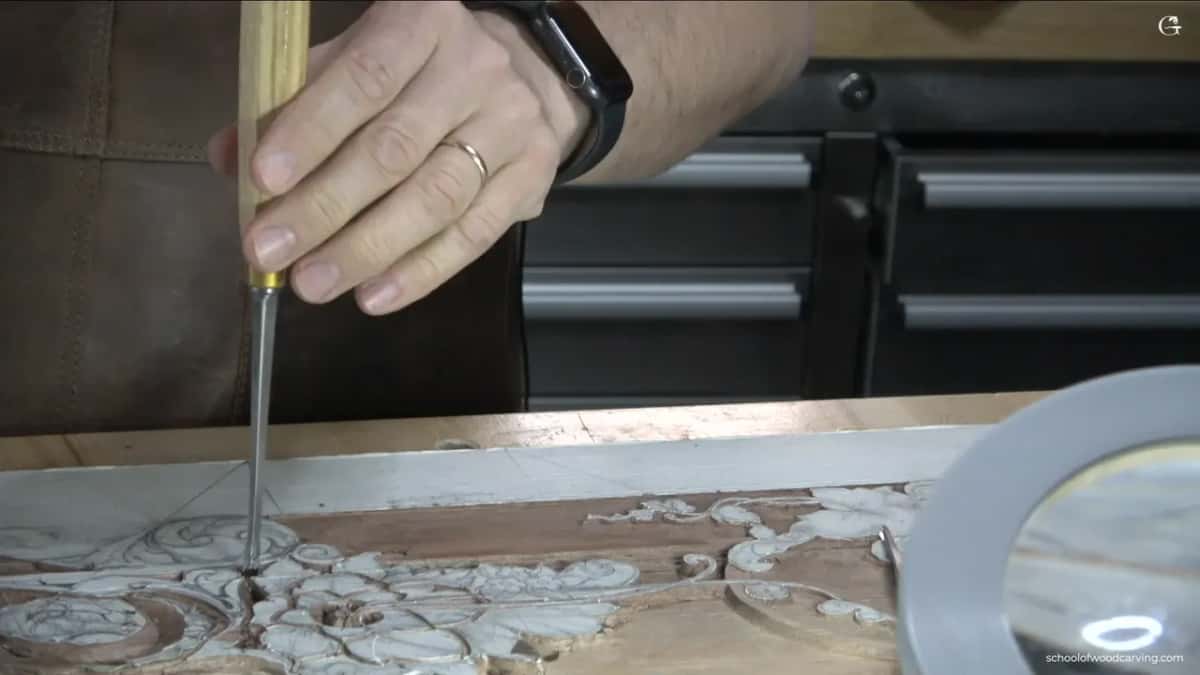 Wedding ring and watch on his wrist, gouge stood upright, mallet waiting above it.