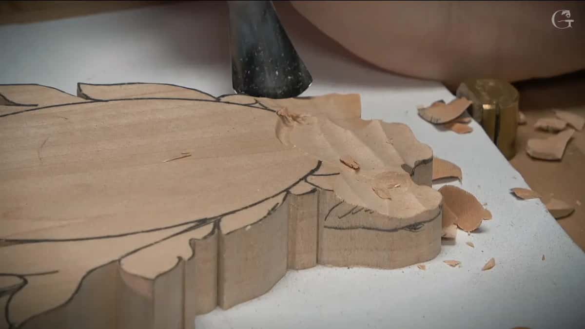 Gouge driven down along the edge of a leaf while shavings scatter across the white board underneath the work