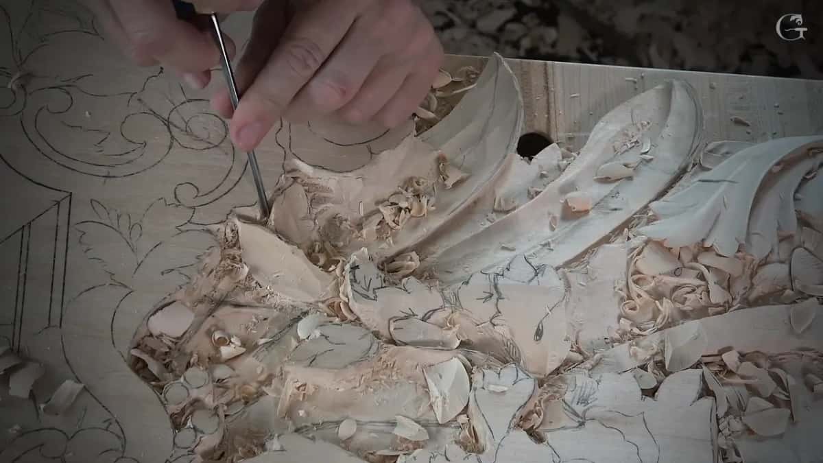 A narrow tool held nearly upright presses down into the leaf area, curls of wood piled all around it