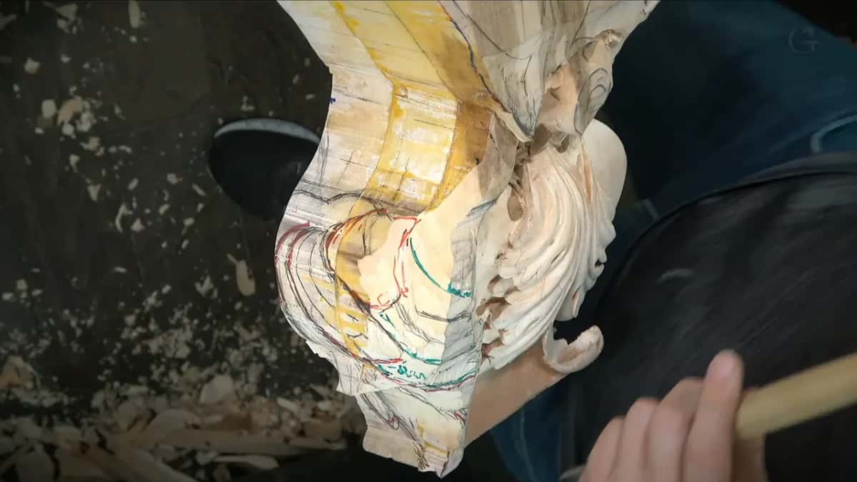 Red and teal lines crossing the carving while a pale tool handle waits at the right