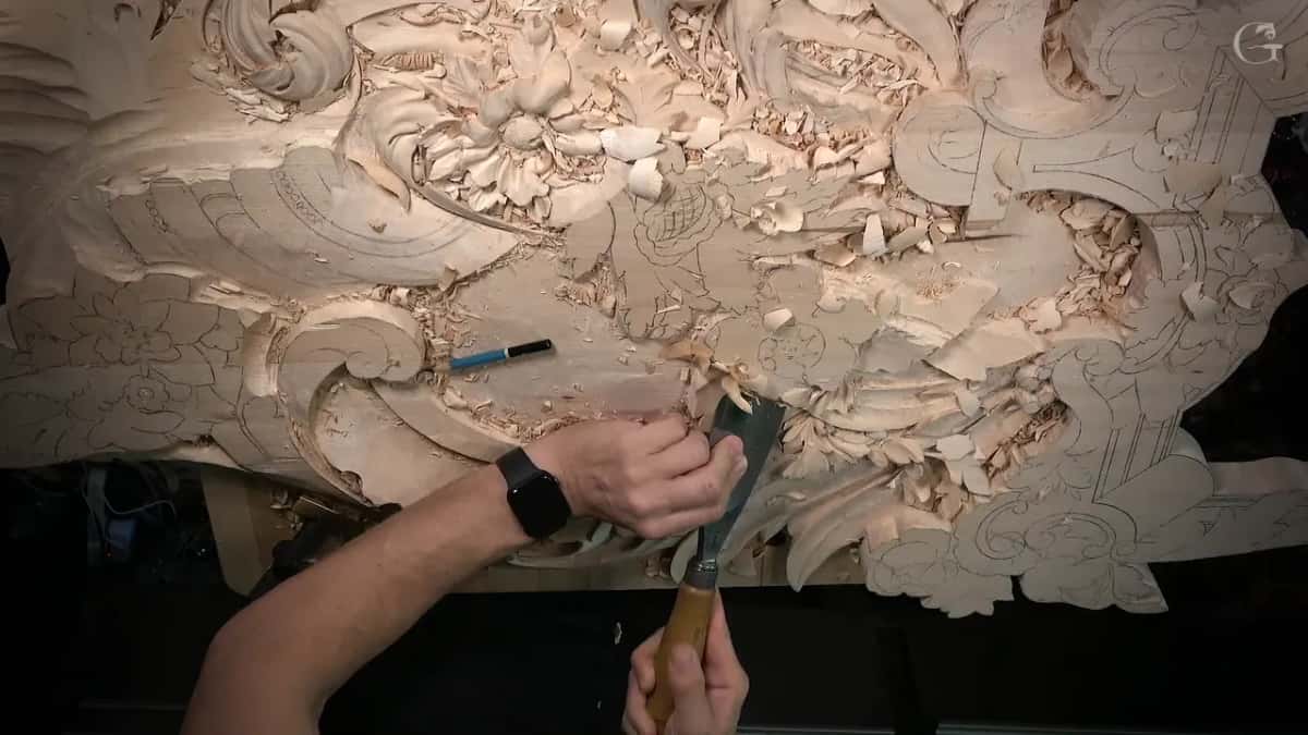 Seen from above, both hands on one gouge and a blue pencil left on the wood