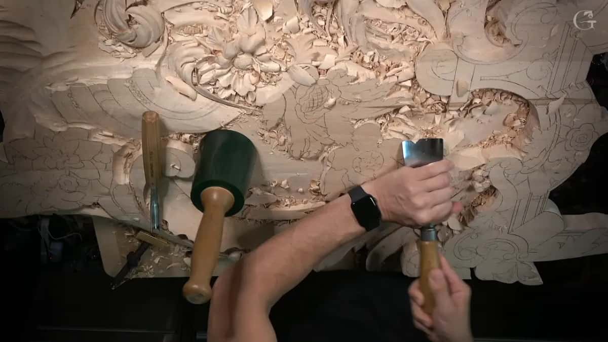 Overhead, both hands steer a wide gouge on the big panel while a green mallet stands nearby