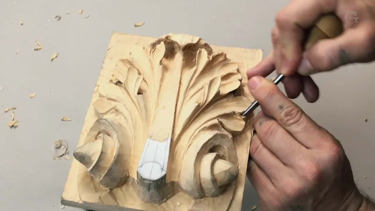 Tattooed hand holding a flat chisel like a pencil, slicing at the shoulder of a leaf