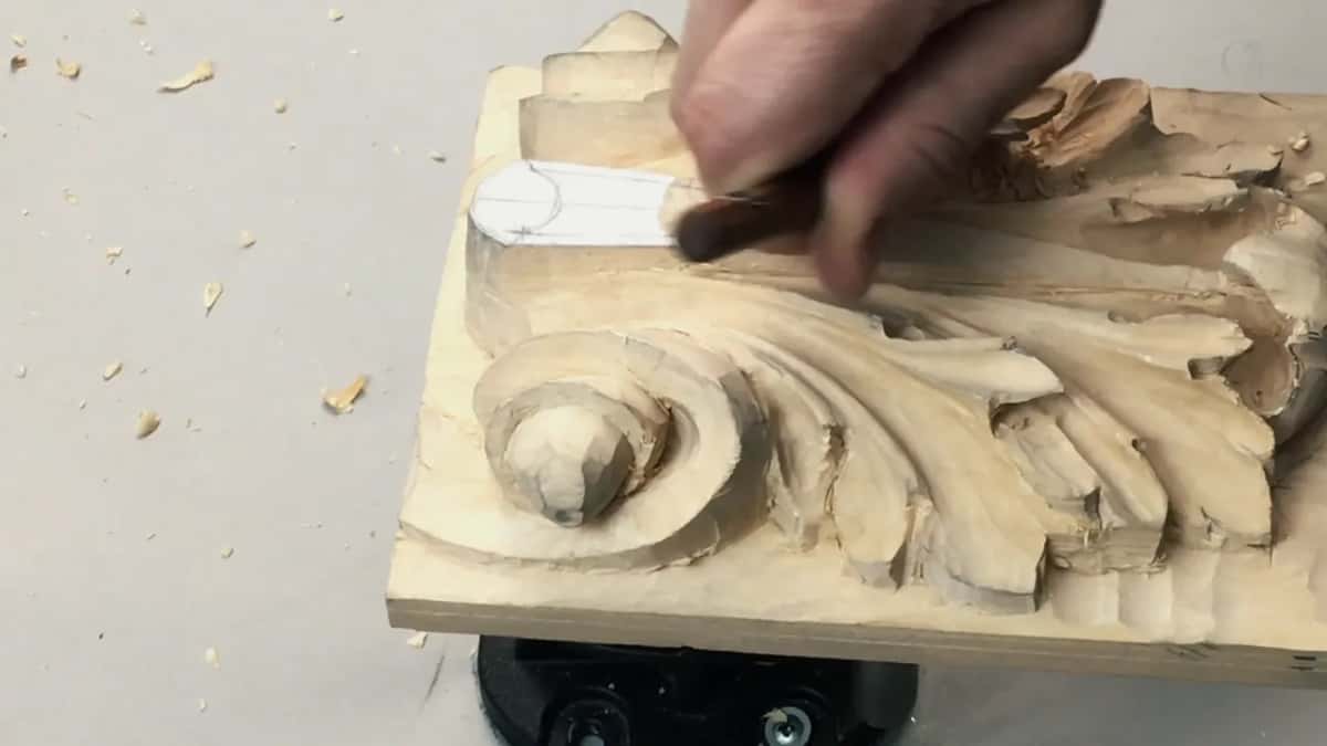 Thumbs braced either side of a small gouge near the head of the carving, shavings scattered beyond