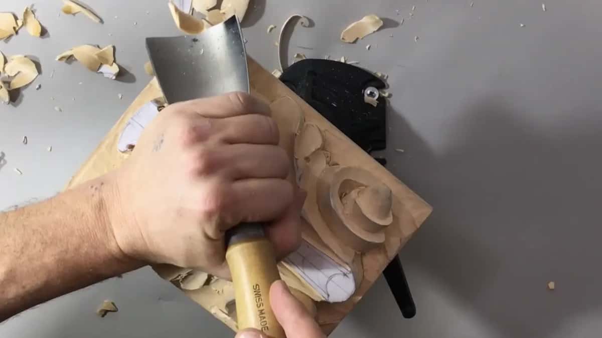 Wide gouge with a long pale handle pressed into the top left corner of the turned board