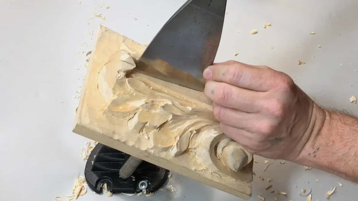 Wide flat chisel blade coming down from the top right of frame, gripped low near the steel