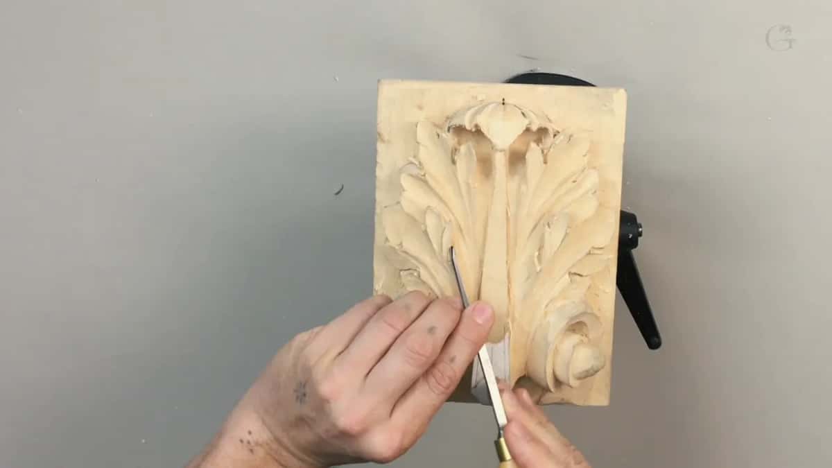Small panel held upright while both hands drive a white handled gouge into the middle of the leaf