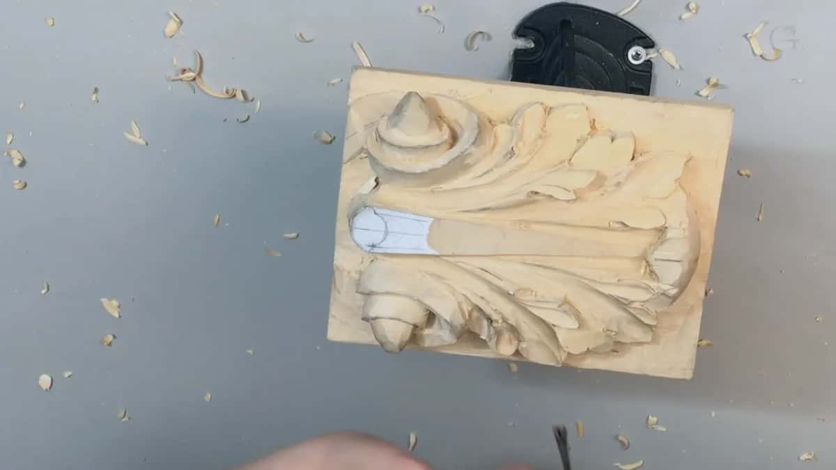 Bare basswood, unfinished, with a white handled tool lying across the carved leaf