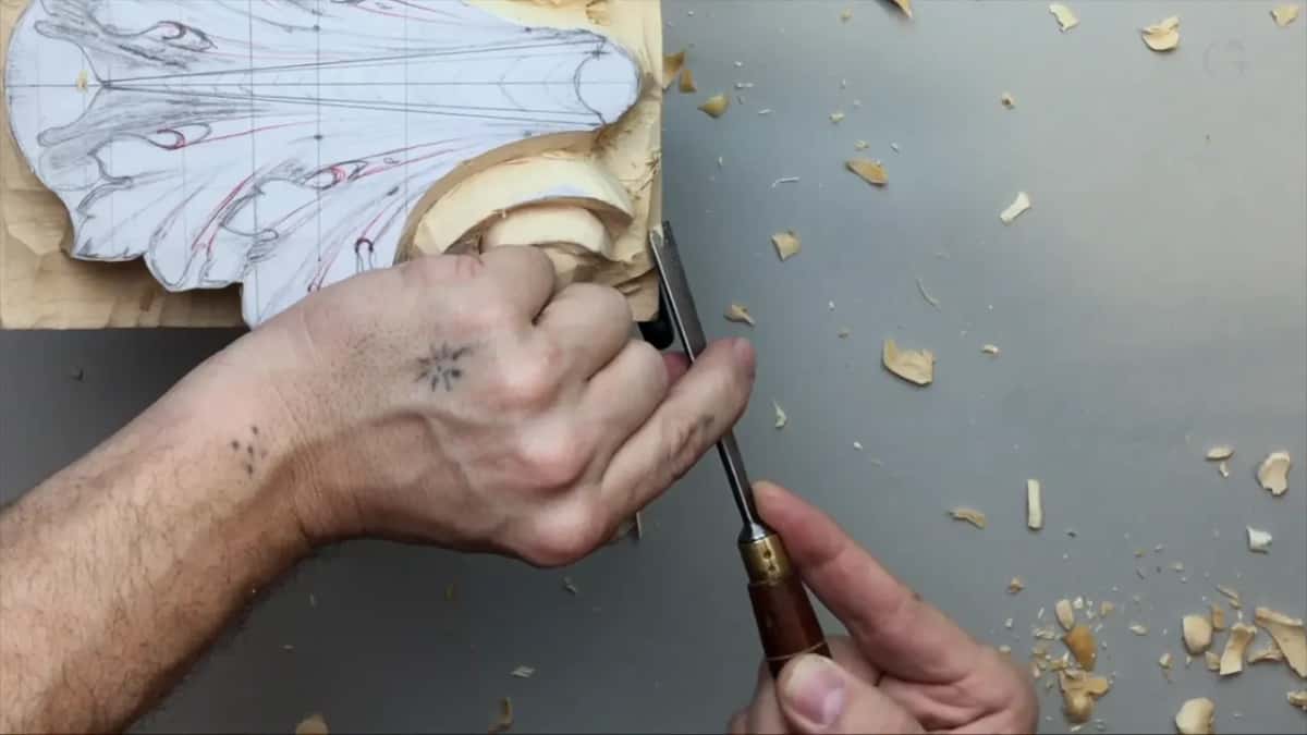 Dark handle in one hand, its blade at a carved volute, chips all over the bench