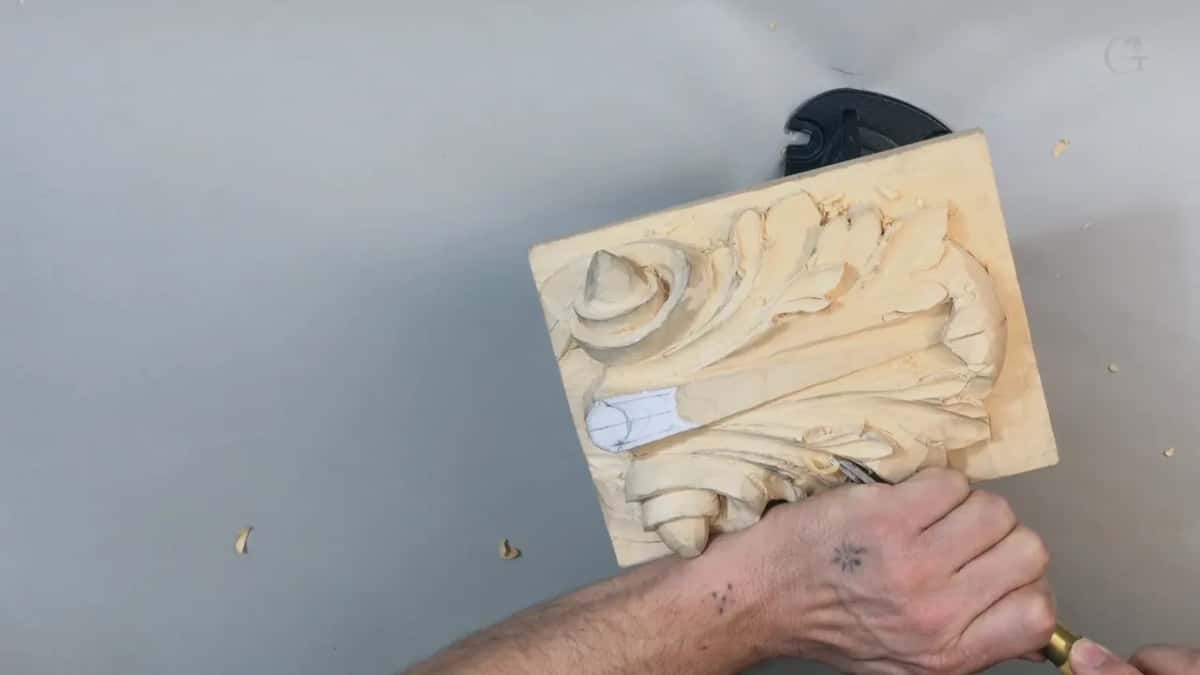 Panel tilted on the round vise base while a hand comes in from the lower right, shavings loose on the table