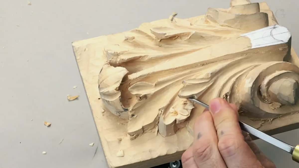 Tilted board with a hand coming in low from the right, curls of basswood across the grey table