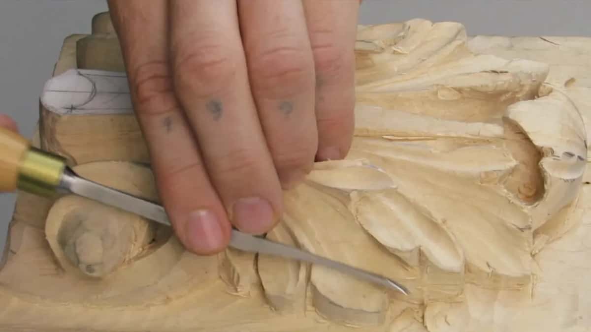 Fingers spread flat over the carving, one blade working the top edge