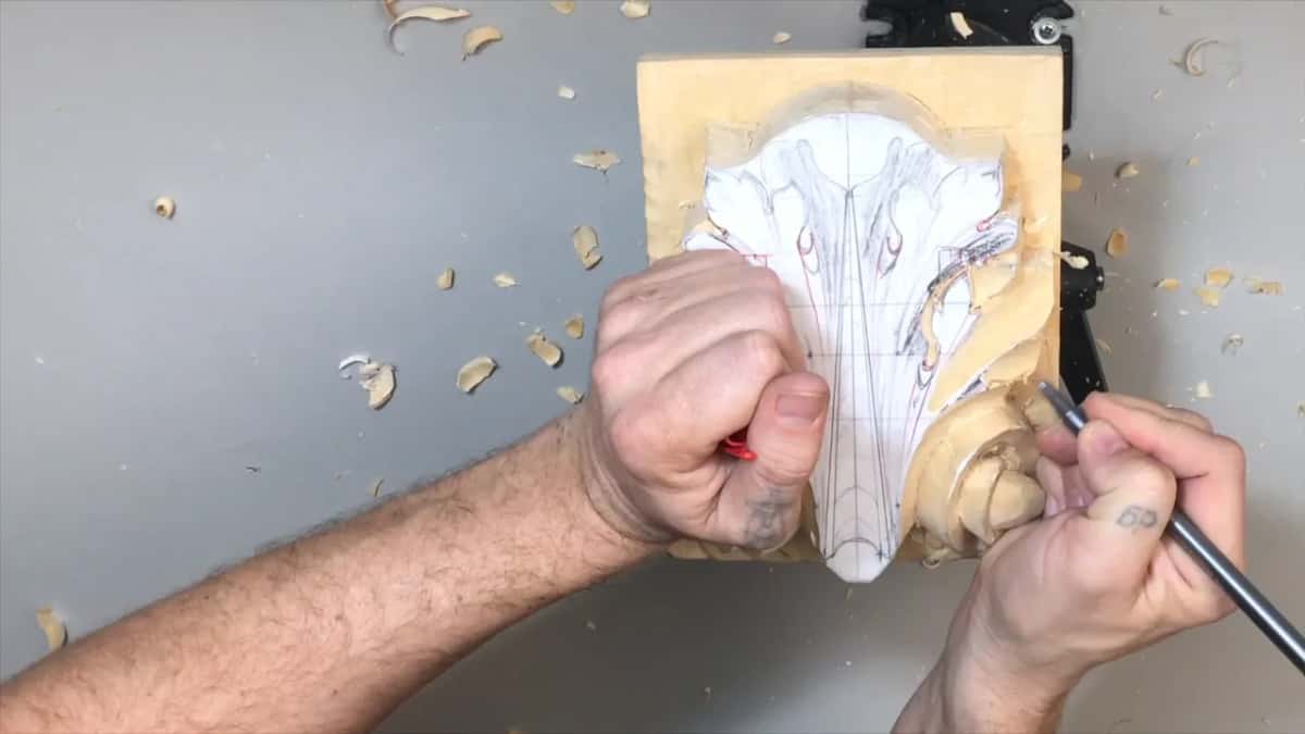 Something red in one fist at the center, a pencil by the right volute