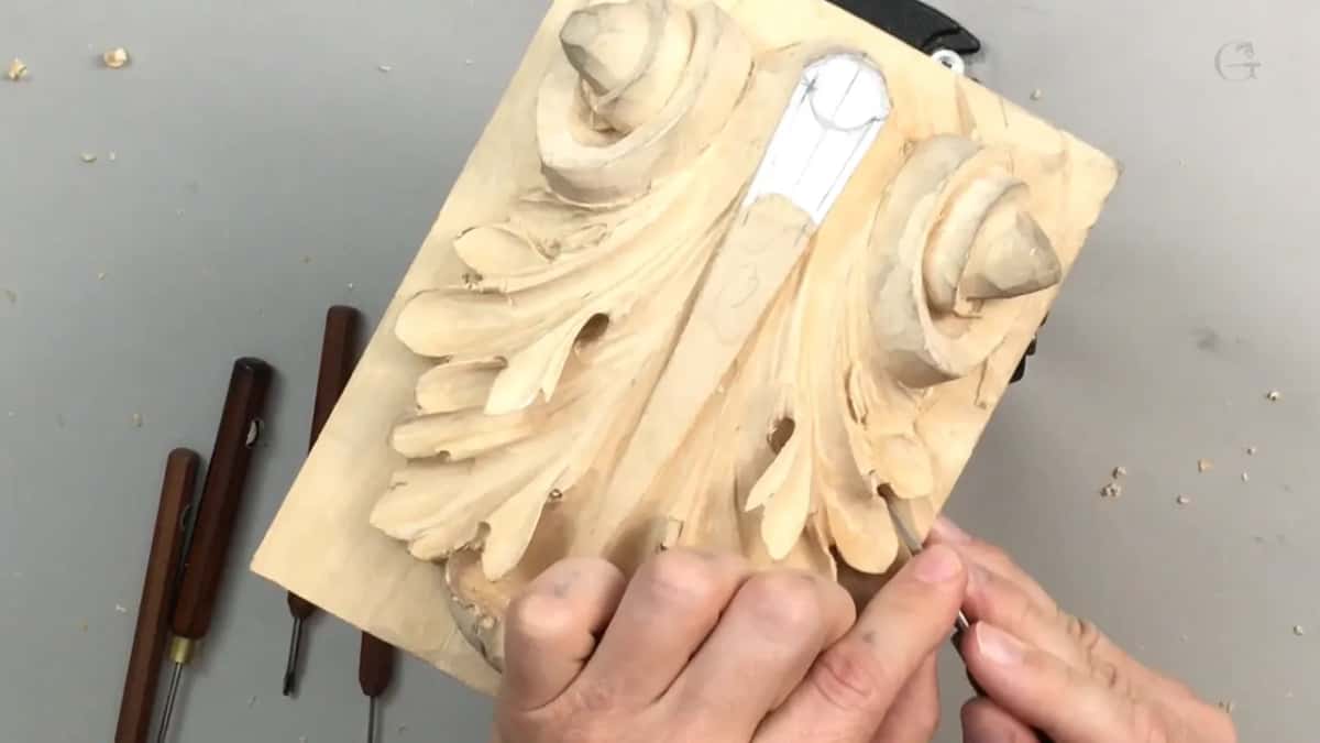 Three brown handles resting on the bench beside the panel while both hands work the lower part of this carving
