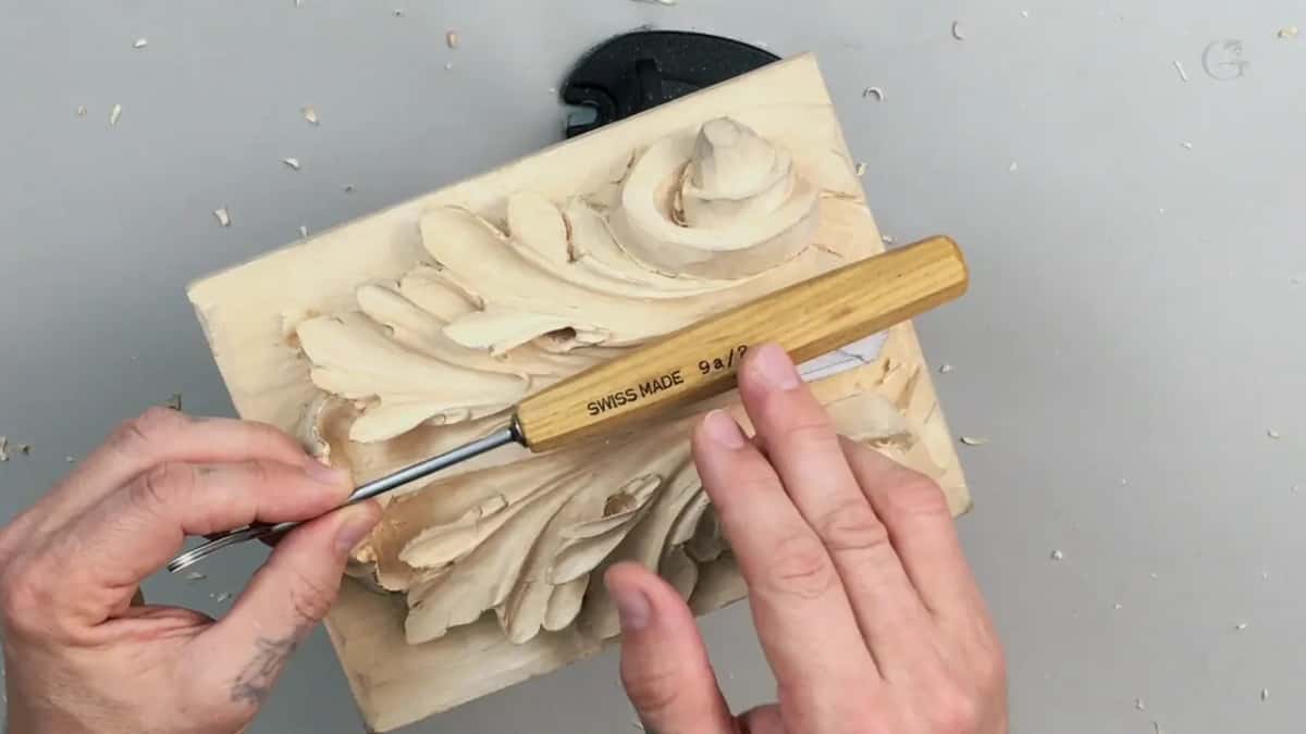 Pale handle stamped SWISS MADE lying across the leaf while the far hand steadies the board