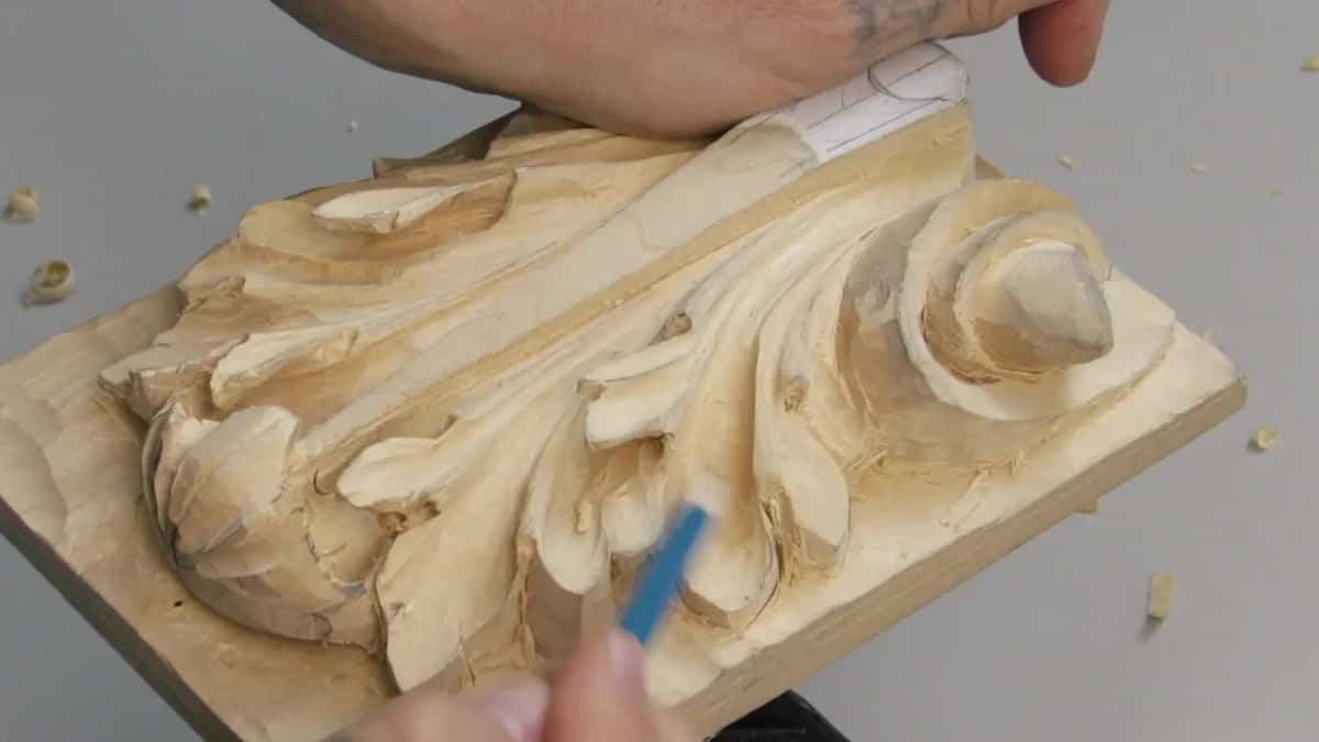 Forearm across the top of the frame and a blue pencil held below the panel, marking where the undercut must stop short