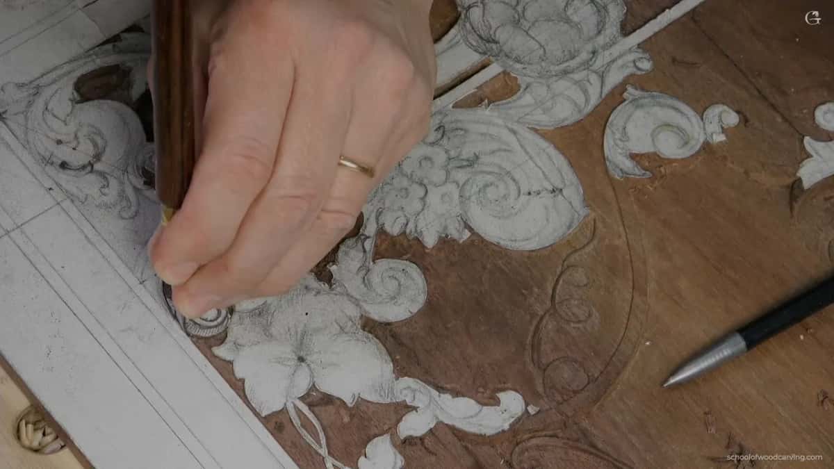 Hand at the carved flowers, a pen lying beside the work.