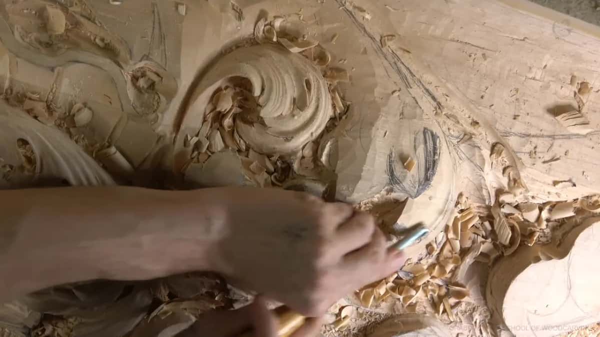 Forearm across the board, gouge beside a pencil-marked ridge.