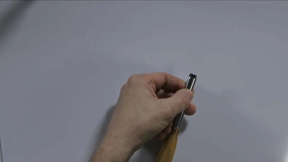 A gouge held upright by the ferrule on a plain white surface, edge at the top