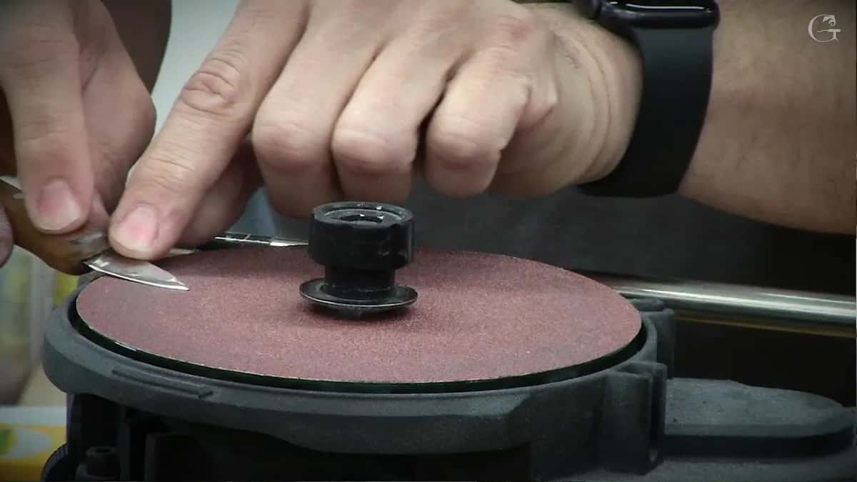 Knife blade laid flat on a red abrasive disc while both hands steady it