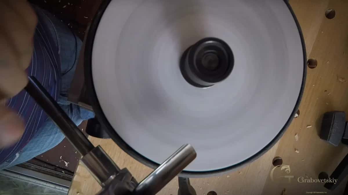 Seen from above, a pale disc spins beside the steel bar of the jig.