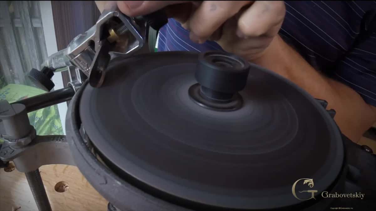 Both hands hold the jig over a dark spinning disc, its bar at the left edge.