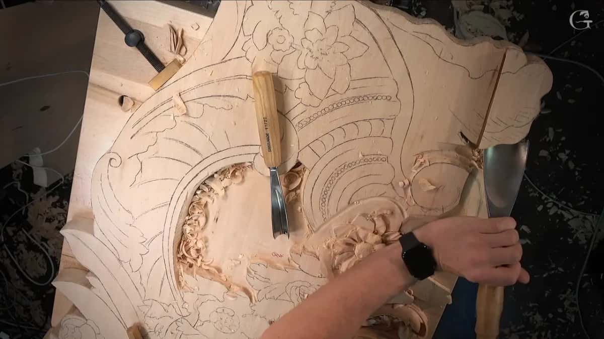 One gouge stands upright in the panel while a hand at the edge holds a wide one