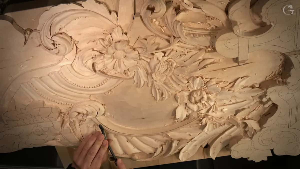Carved flowers across the top, one hand reaching in from the lower left with a tool