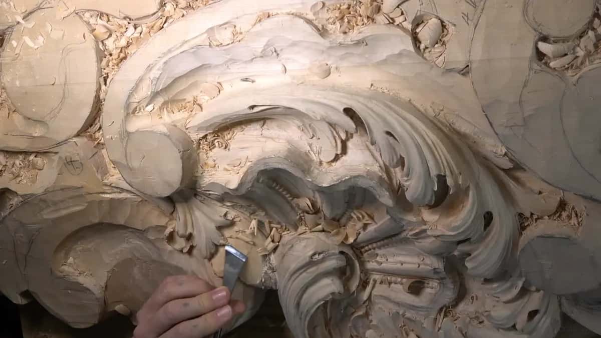 A skew chisel works low on the panel, below the big scroll.