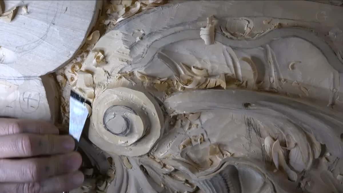 A flat, shiny blade touches the volute's left side among the shavings.