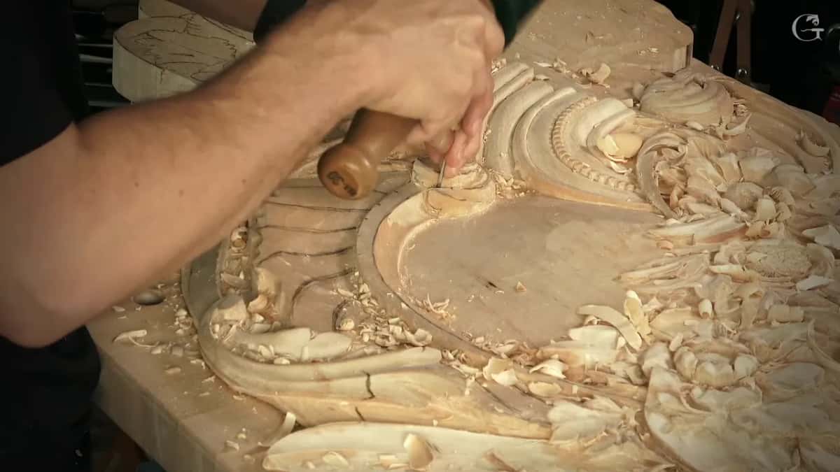 Low side view of a hand pressing a round handled tool into the scroll, chips all over the board