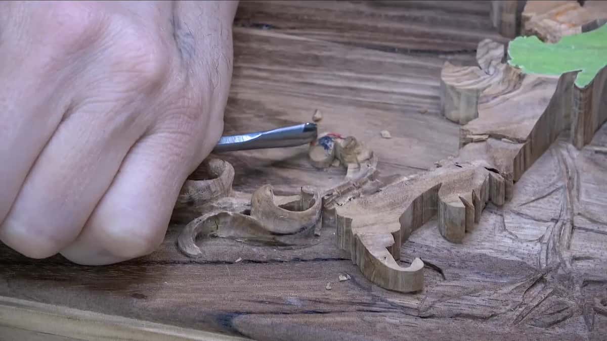A fist holding a gouge comes in at the second scroll from the left, knuckles low over the lid