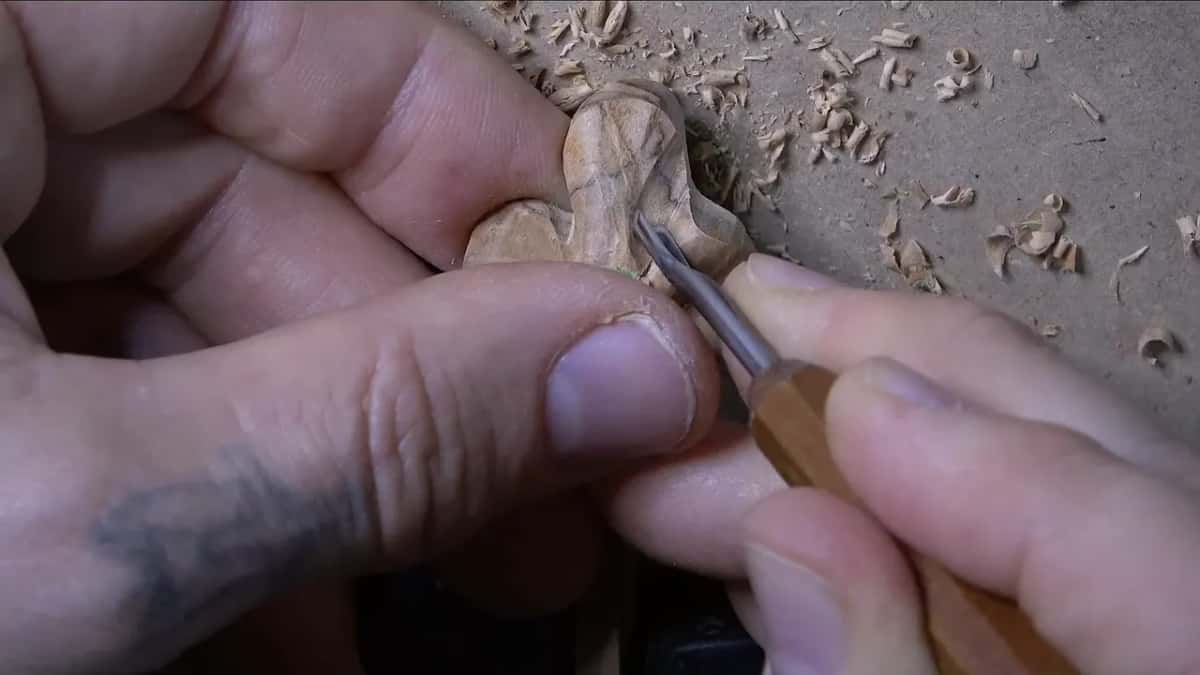 Gouge with a pale handle deepening one petal while a thumb braces the flower