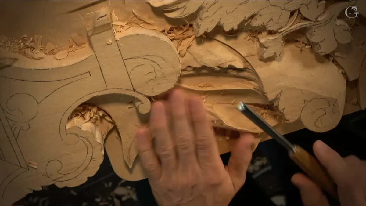 Palm flat on the scroll while the other hand drives a flat gouge into the leaf