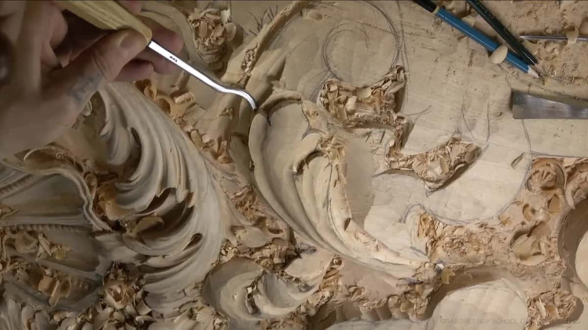 A spoon gouge with a long curved shank reaches into the leaf while pencils and a flat chisel rest nearby.