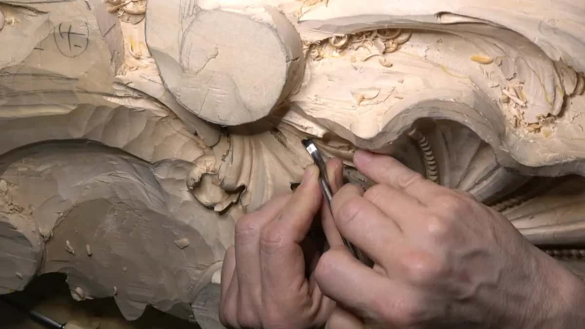 Two hands guide a spoon gouge into a tight spot between leaf parts.