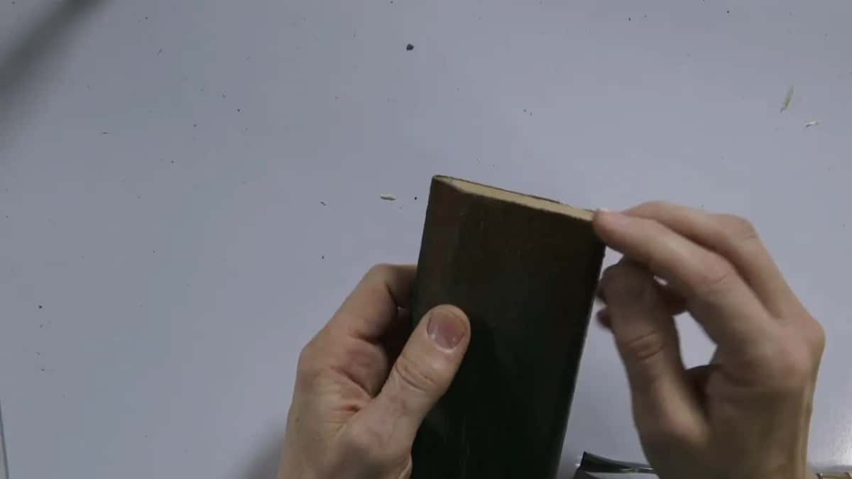 Held up in both hands, a block of wood with a dark face, almost black.