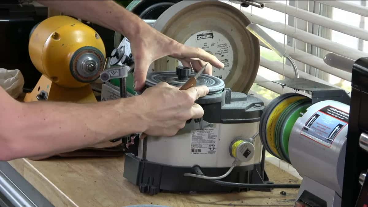Two hands bring a carving knife to the wheel, the Tormek standing behind the machine.