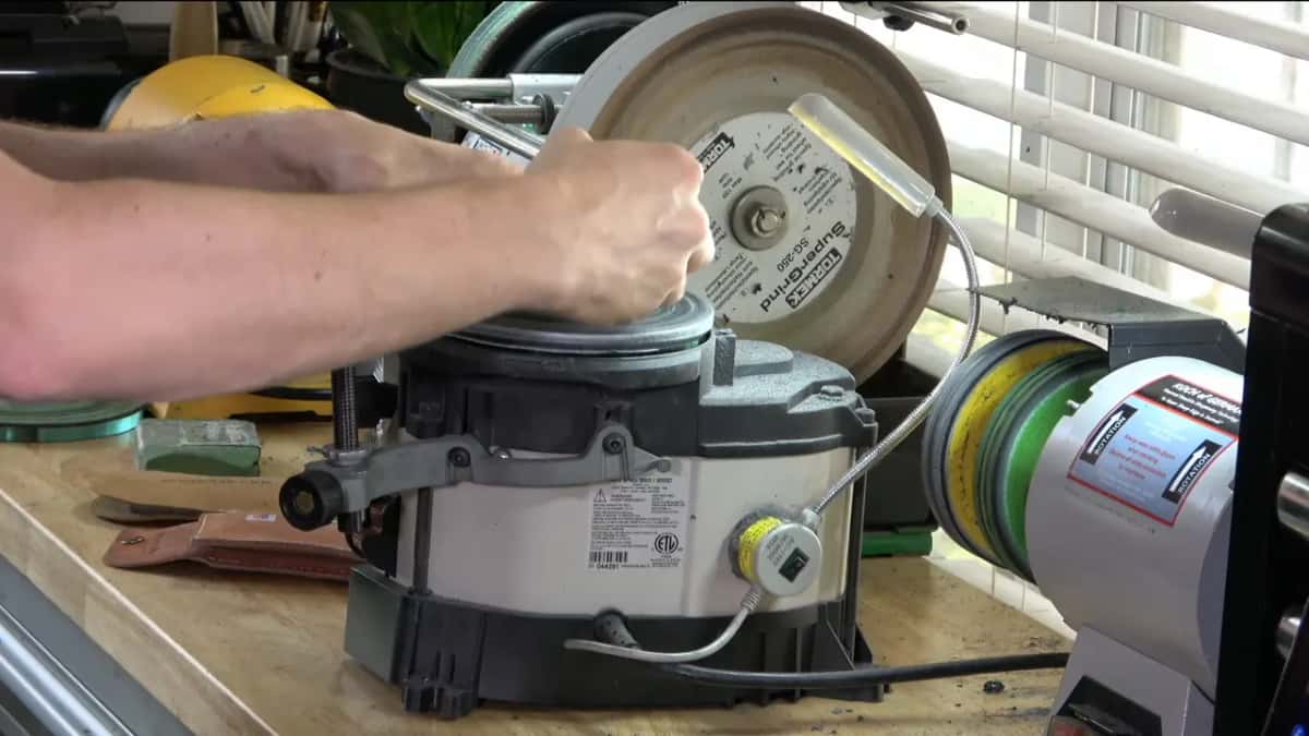 Work Sharp in the foreground, Tormek wheel behind it, with a green compound bar and a strop on the bench.