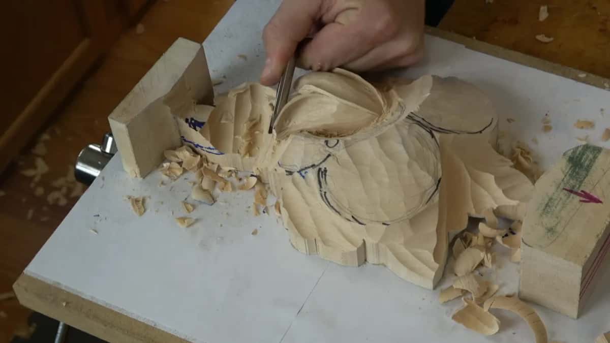 Both hands turning the tool onto its side to start undercutting the flipped petal, wrist braced on the board