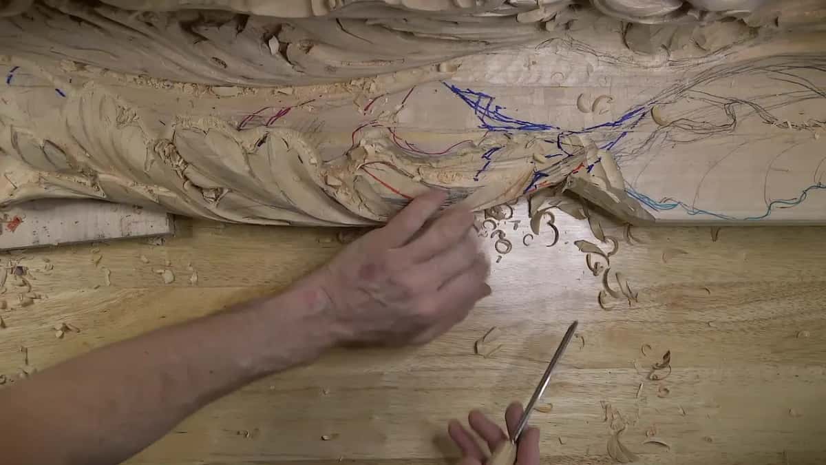 One hand rests on the thin carved section while the other holds a slim steel tool near the bench