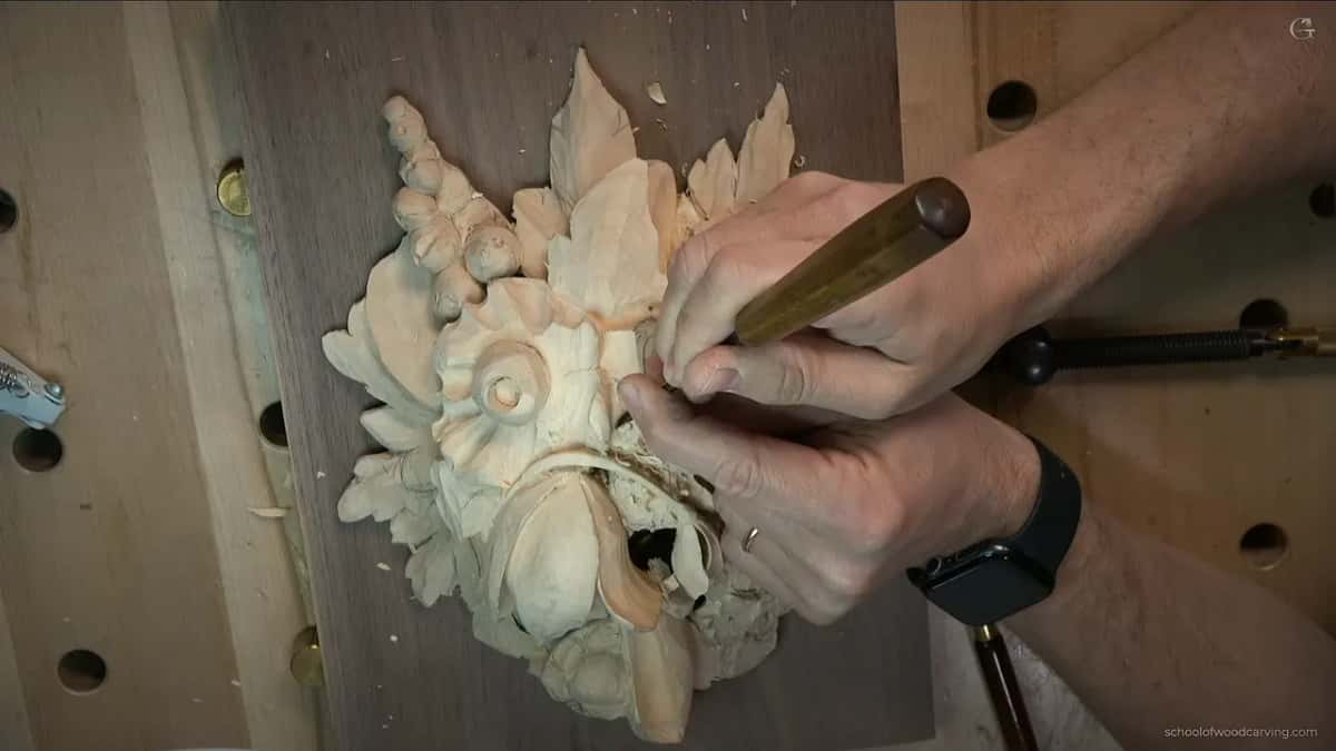 The tool resting across one finger while the other hand steers it near the tulip, a watch on the wrist