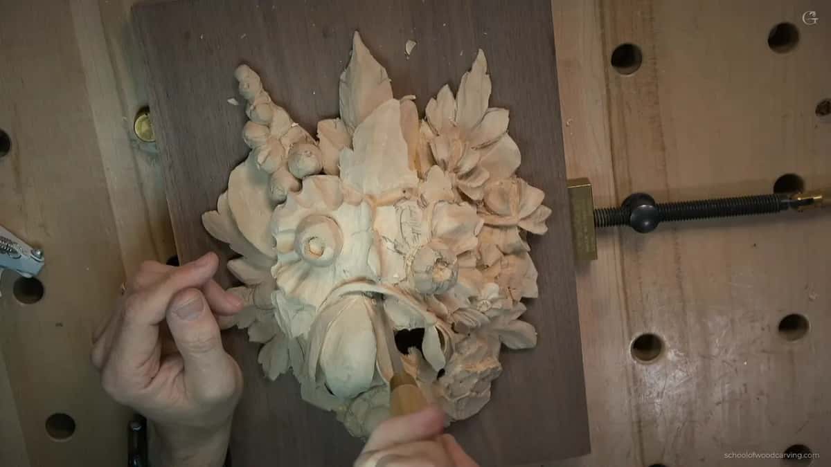Seen from above, a hand holds the tool right at the new opening, the walnut showing dark through it