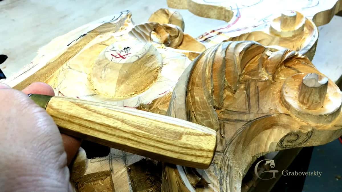 Octagonal handle and its blade laid against a gilded carved panel that is still in progress on the bench.