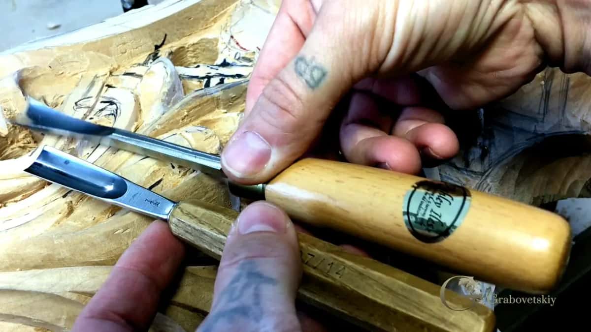 Maker's label printed on a round handle, two more tools resting on the carving beside it.