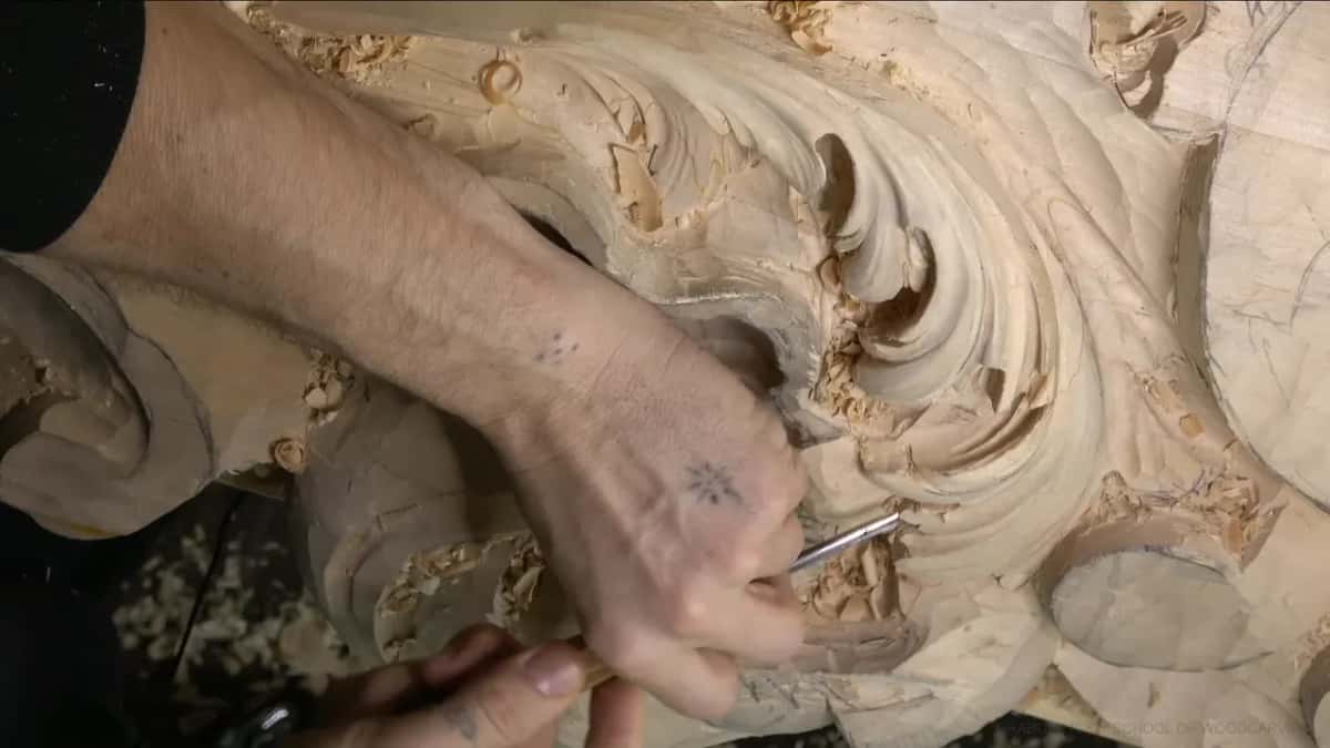 Two hands steer a narrow gouge under a curl.