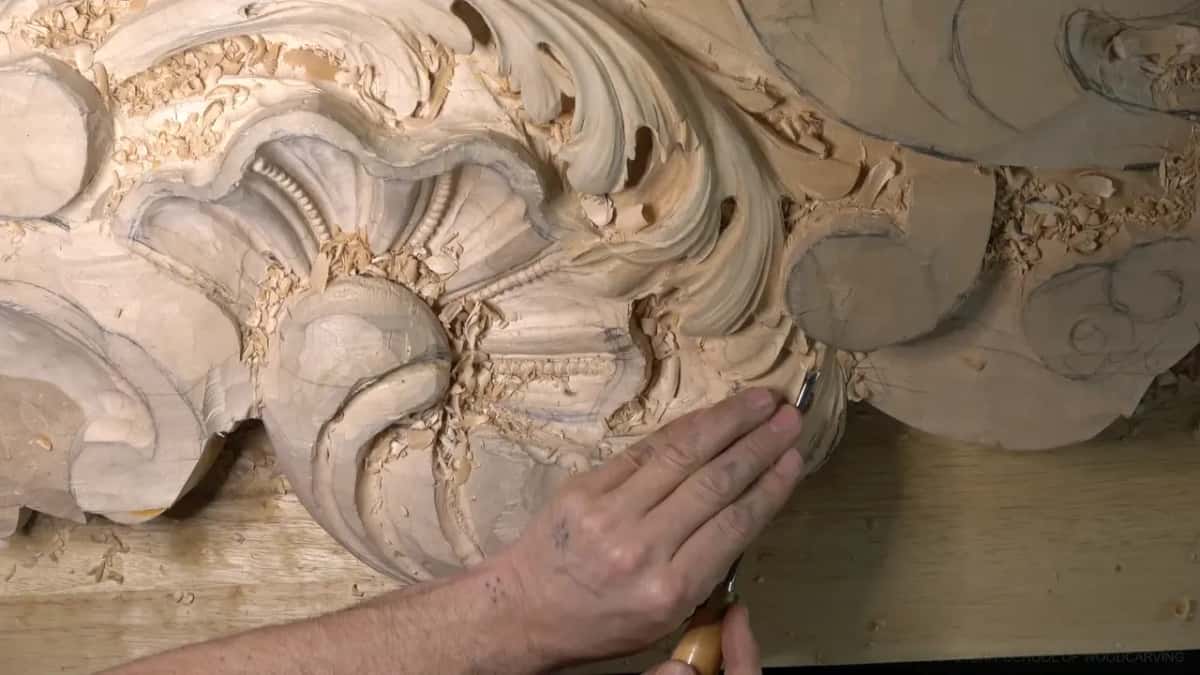 His palm braced flat on the shell while the other hand pushes a small gouge under a leaf edge.
