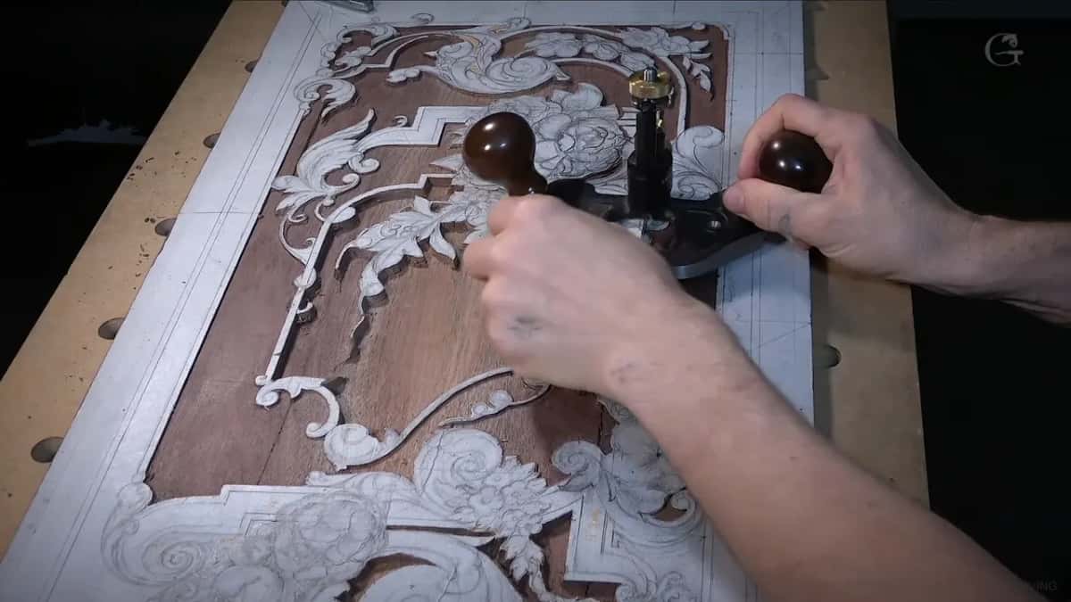Both hands on the router plane close over the board, with the ornament still chalked white against brown wood