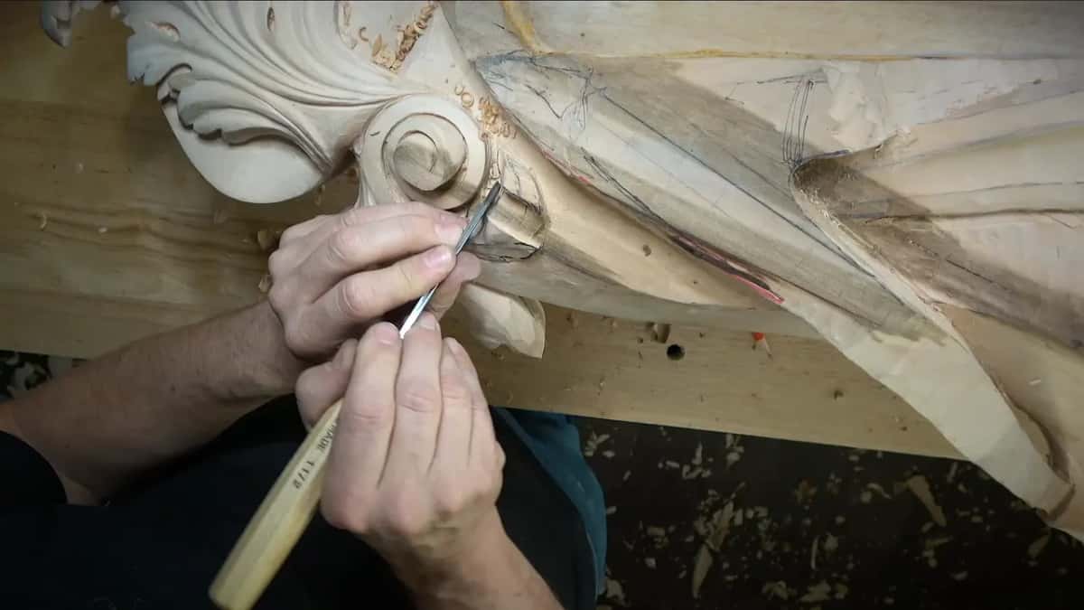 Both hands guide the narrow tool along a drawn line next to the volute