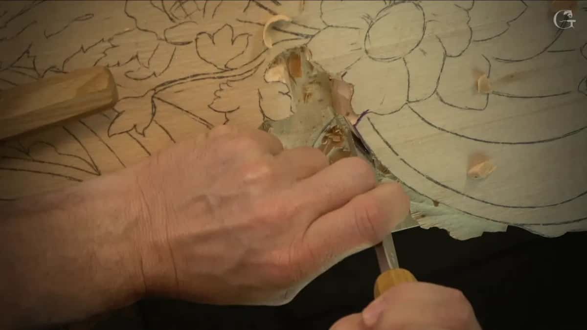 Near the flower drawing one hand steadies a chisel on the new wall while a wood handle lies at left.